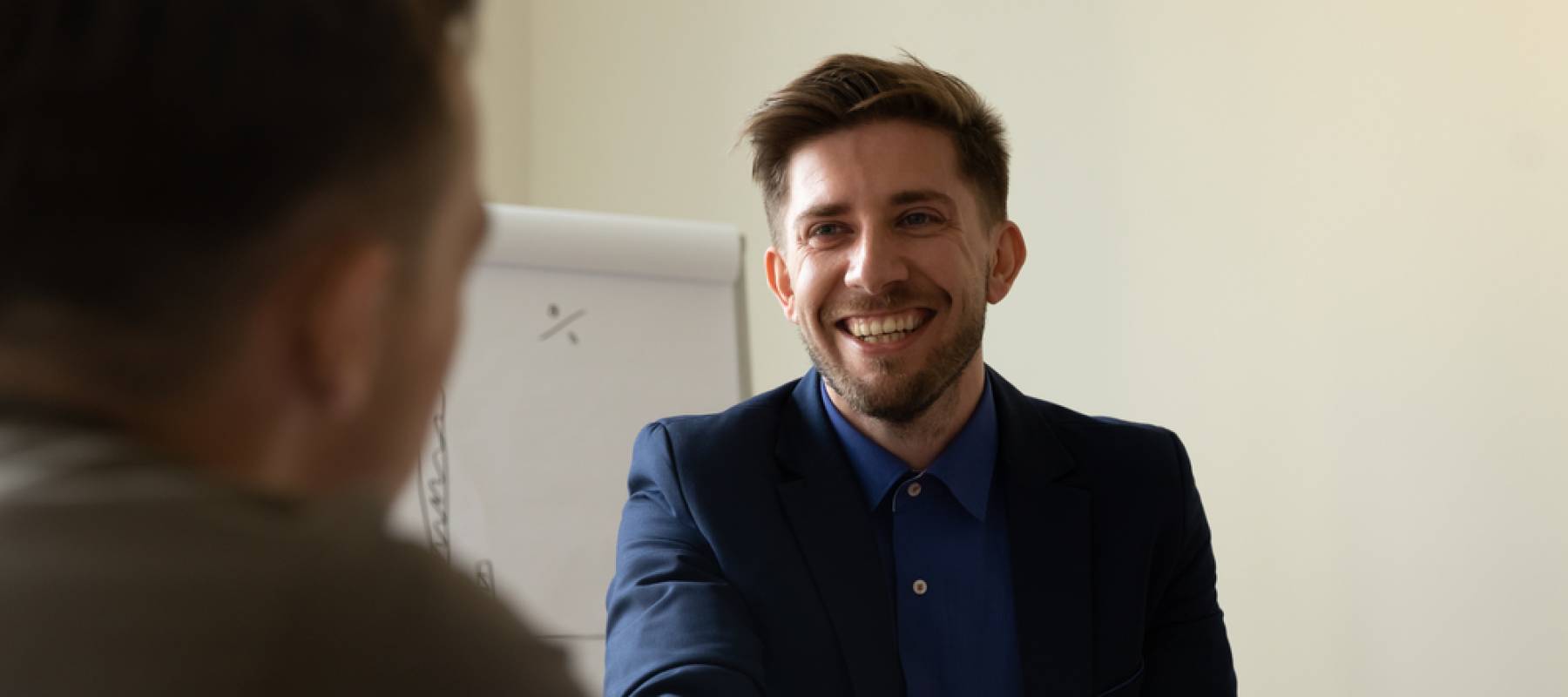 Smiling young man shakes hands with someone facing him.
