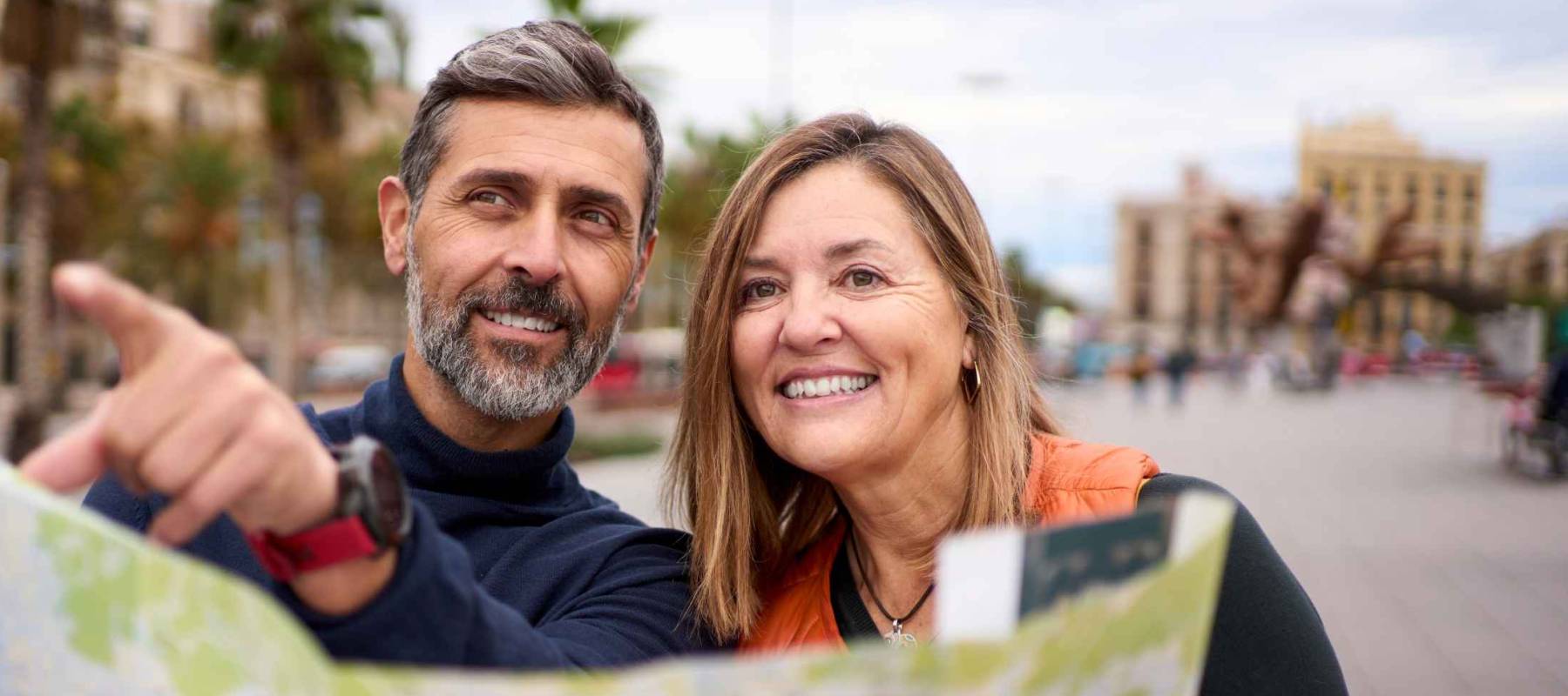 Middle-aged Caucasian couple with travel map in hands looking and pointing places of tourist interest.