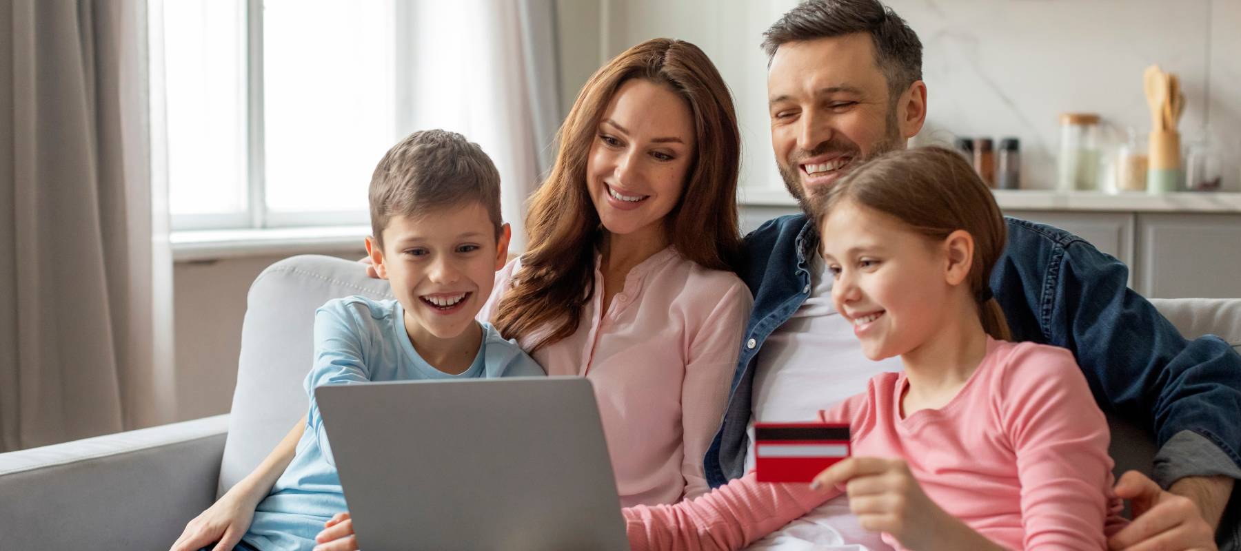 A family of four is engaged in online shopping as one of the children holds a credit card while looking at a laptop