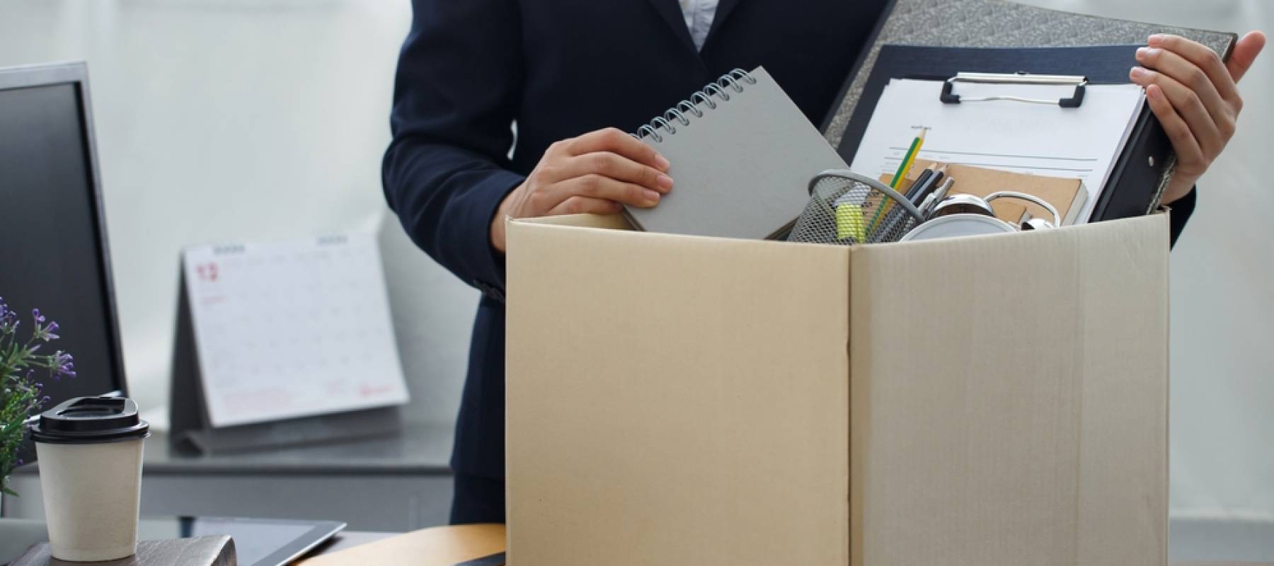 Close up of cardboard box with a person's hands packing it full of office supplies.