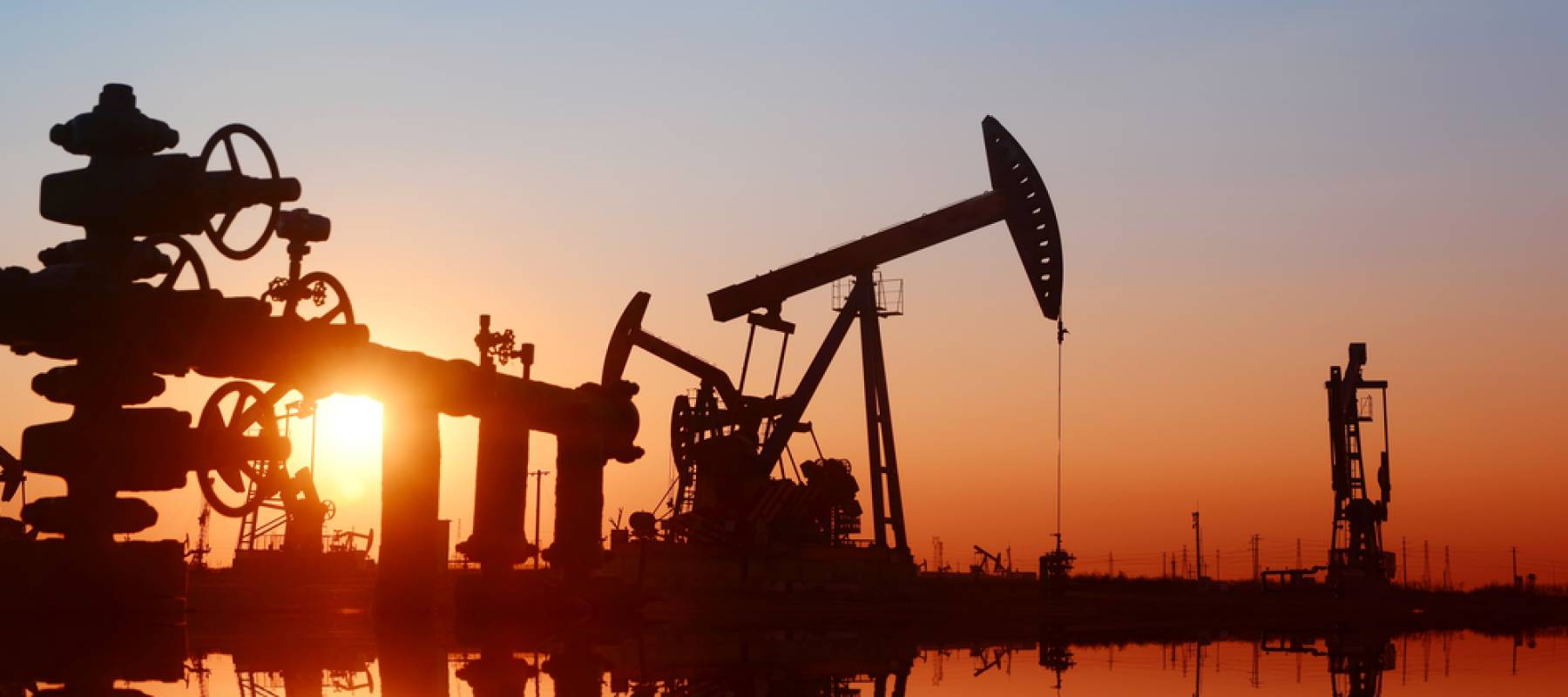 Working pumping unit in oil field seen in shadows in front of a colorful sunset.