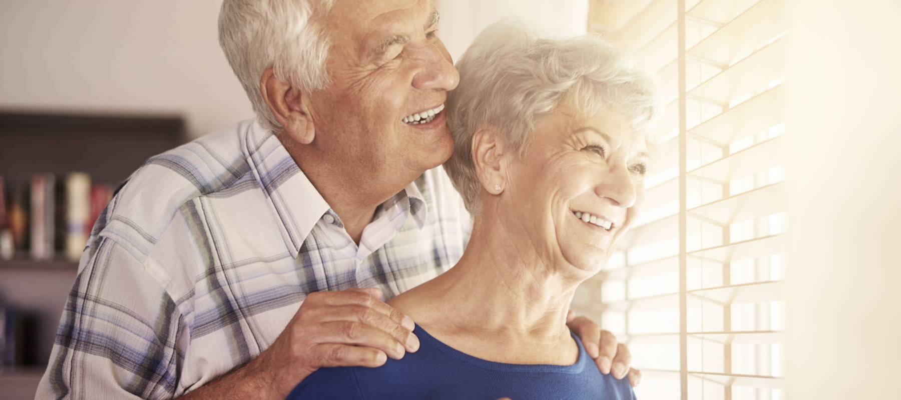 Older couple hugging by a window in their home