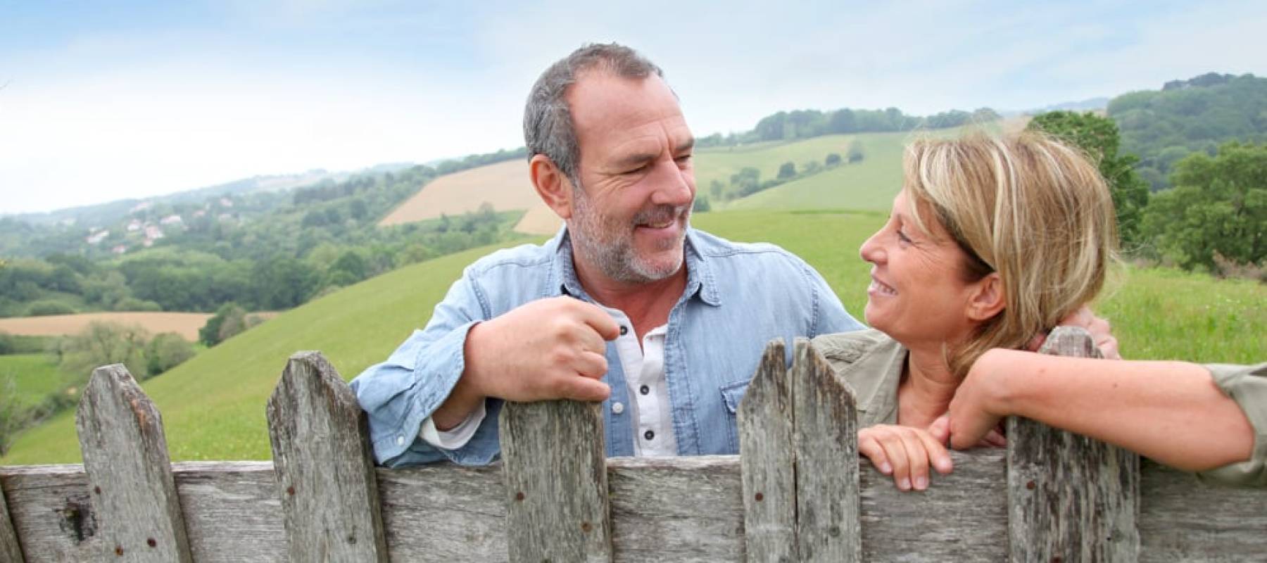 Senior couple leaning on fence in countryside.