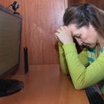 Woman with her head in her hands sits in front of a computer.