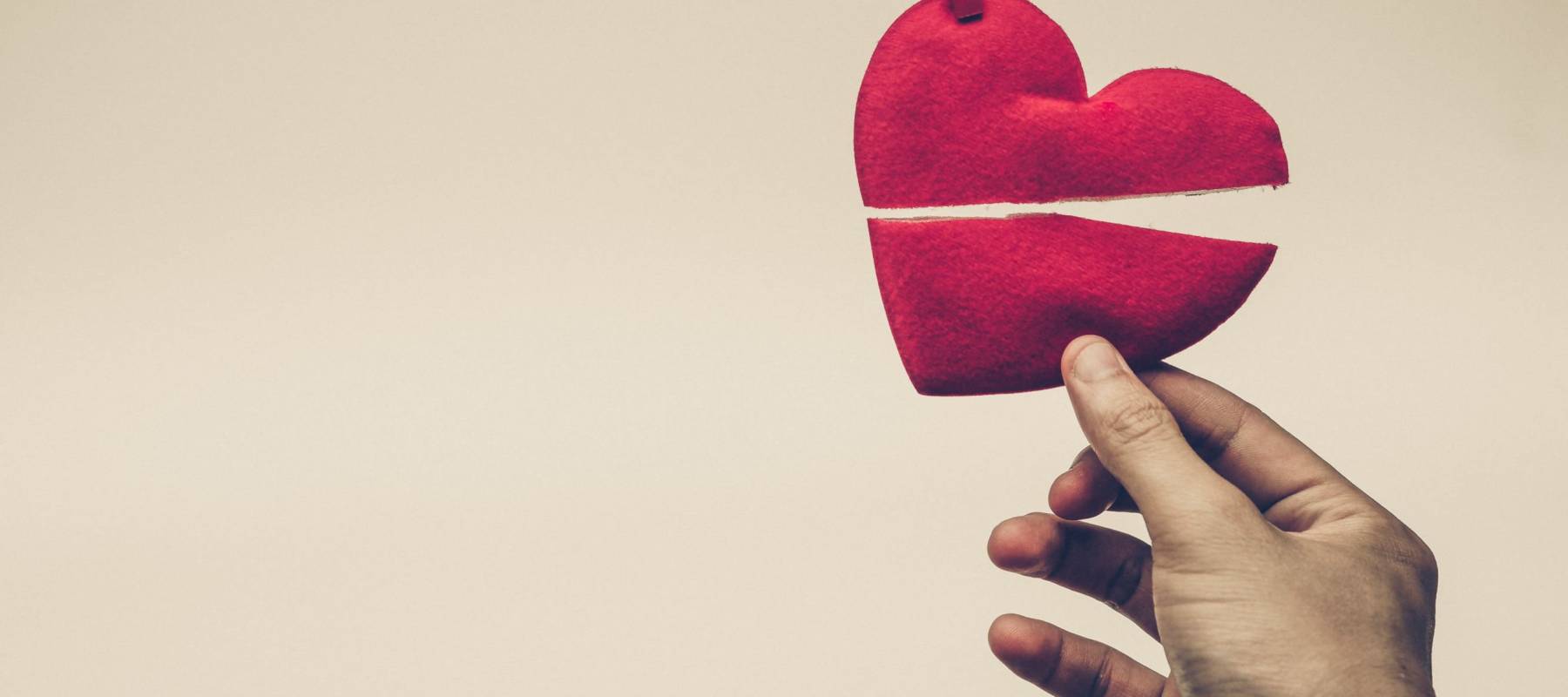 hand holding broken red heart hung on rope