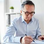 business, people, paperwork and technology concept - businessman with calculator and paper working in office