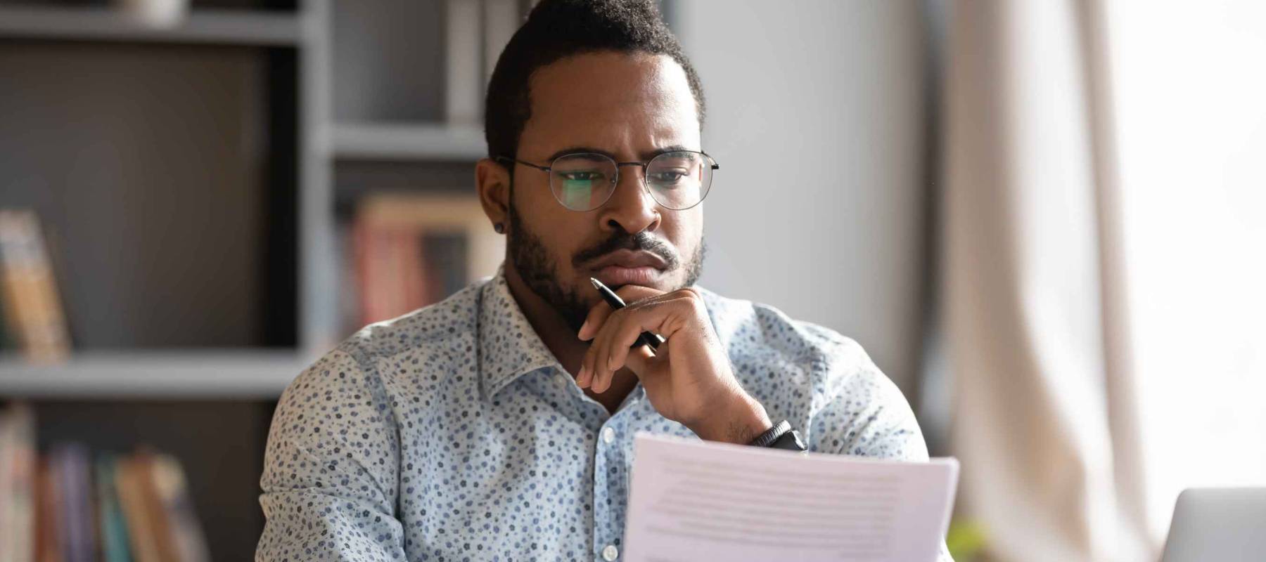 African student guy sits at desk holding papers