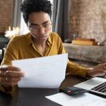 Focused young African American woman in eyeglasses looking through paper documents