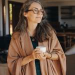 Senior woman looking away thoughtfully while standing with a cup of tea in her hands.
