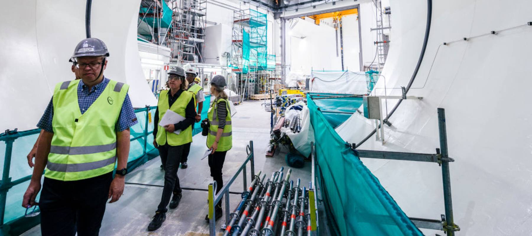 Several workers wearing hard hats and hi-vis vests walking in front of the service gate of the OL3 reactor at the construction site of the Olkiluoto-3 nuclear power plant.