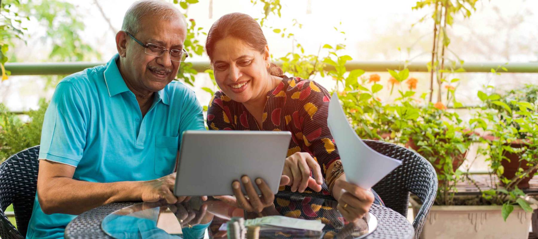Senior Indian/asian couple accounting, doing home finance and checking bills with laptop, calculator and money while sitting on sofa/couch or dining table at home