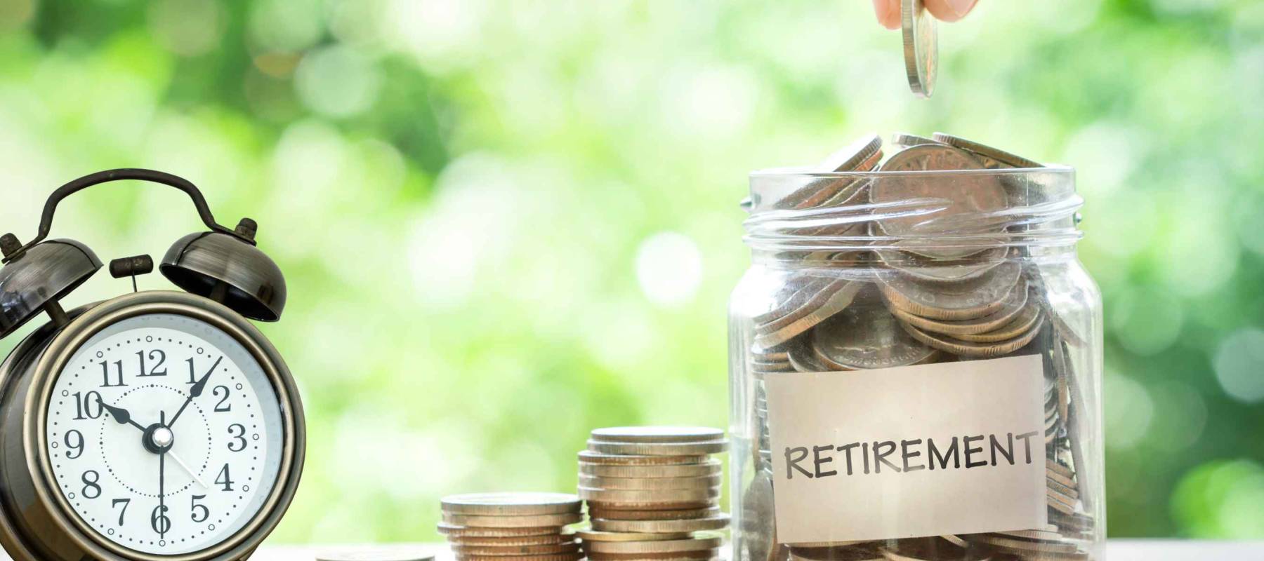 Hand putting Coins in glass jar for with retro alarm clock  for time to money saving for retirement concept