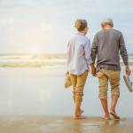 Senior couple walking along a beach, holding hands.