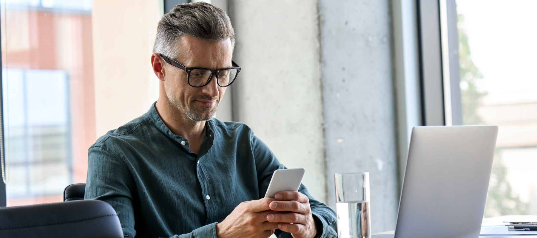Smiling mature businessman holding smartphone sitting in office.