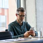Smiling mature businessman holding smartphone sitting in office.