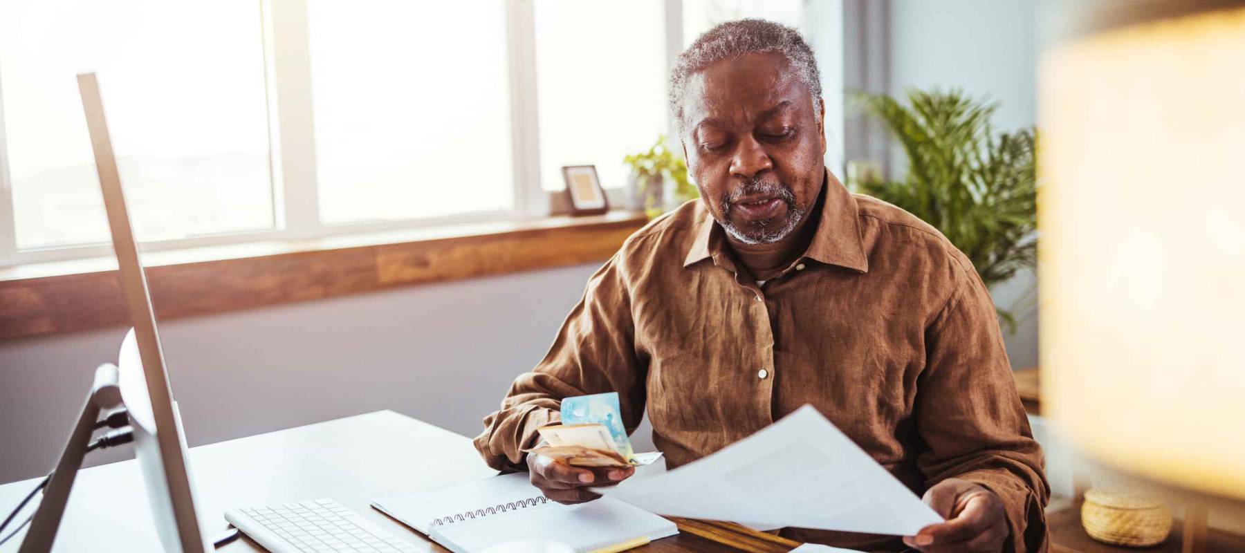 Senior man working at PC computer at home. African American man calculating finances. Shot of a mature man going through some paperwork at home