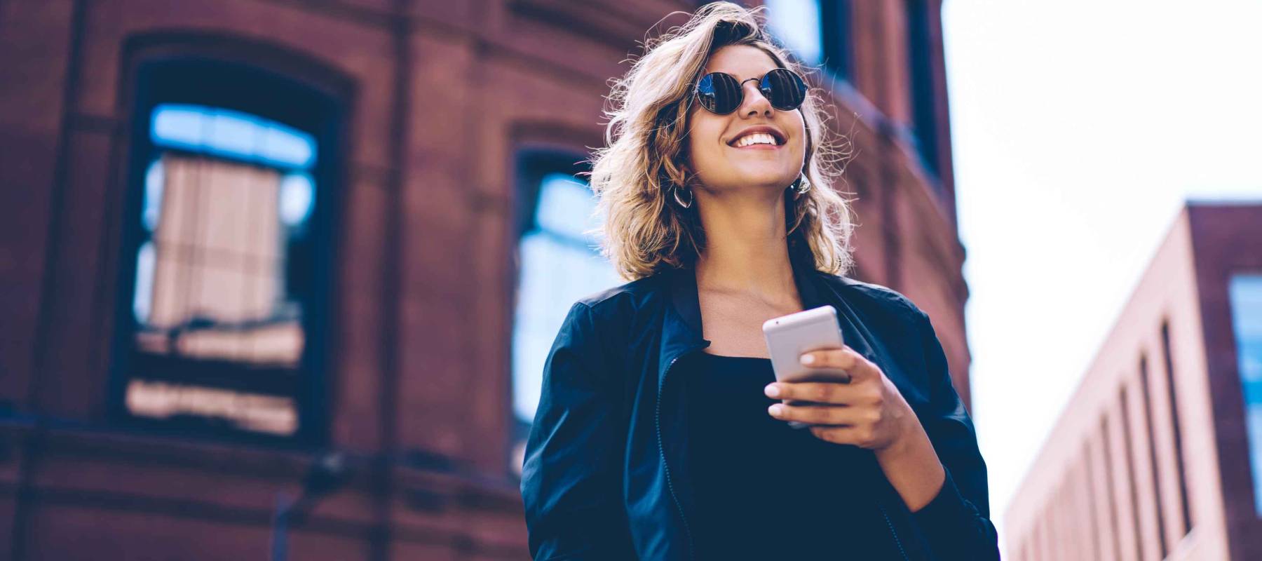 Happy millennial hipster girl in sunglasses laughing on urban setting