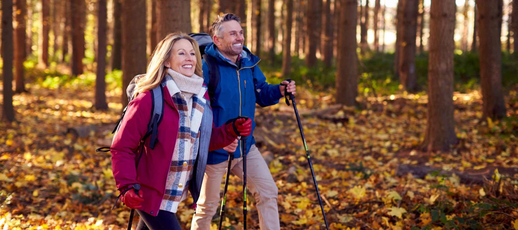 Side View Of Mature Retired Couple Walking Through Fall Or Winter Countryside Using Hiking Poles