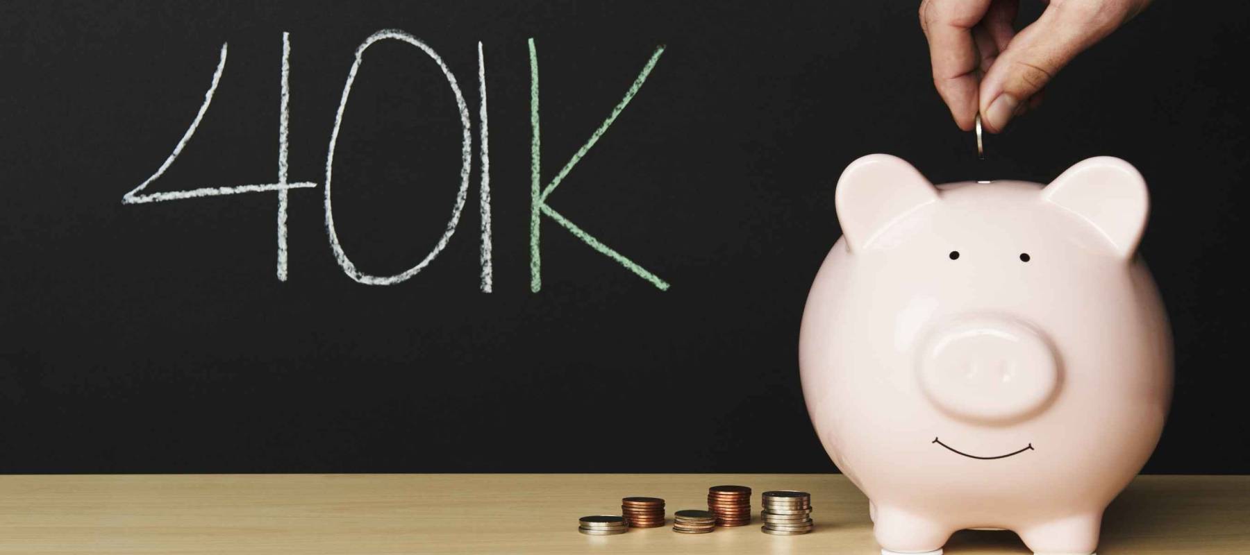Piggybank with 401k written on a blackboard in the background. Money beside the piggybank with a hand putting a coin in.