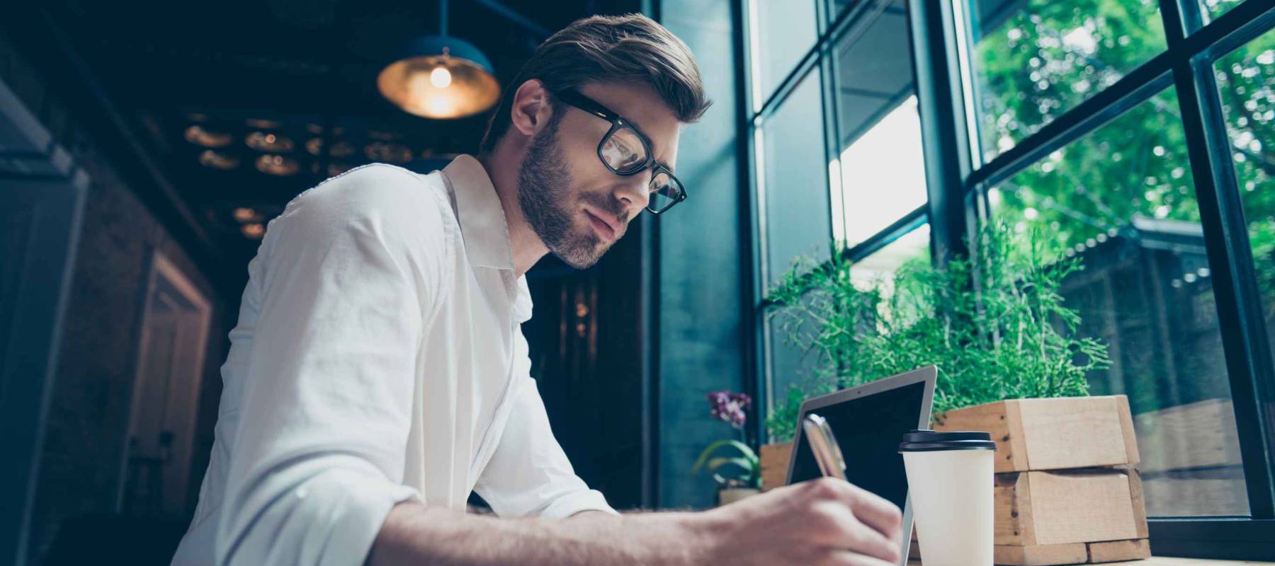 Yow angle view of a young stylish well dressed author writer is working in a modern coworking, writing the novel, in glasses, so serious and focused