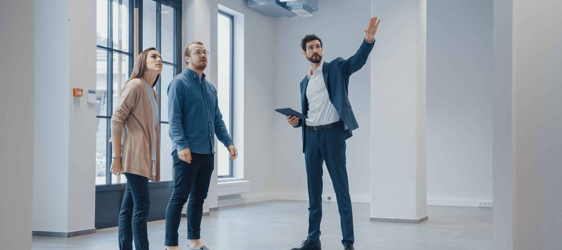Real Estate Agent Showing a New Empty Office Space to Young Male and Female Hipsters. Entrepreneurs Meet the Broker with a Tablet and Discuss the Facility They Wish to Purchase or Rent.