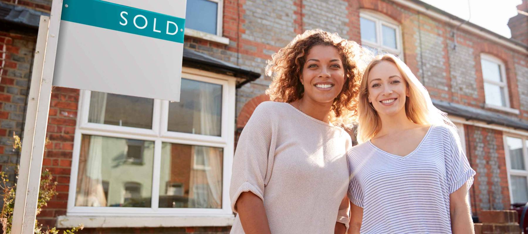 Portrait Of Two Women Standing Outside New Home With Sold Sign