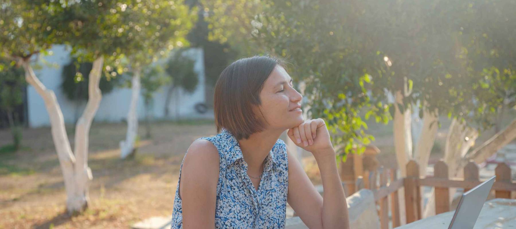 Happy young asian woman with laptop resting outdoors in tiny house in summer garden, weekend away and remote office idea, early morning. Tiny houses and Small Living concept.