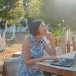 Happy young asian woman with laptop resting outdoors in tiny house in summer garden, weekend away and remote office idea, early morning. Tiny houses and Small Living concept.