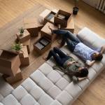 Top view happy couple tenants homeowners relaxing on couch on moving day in living room with cardboard boxes, man and woman resting after relocation in first own apartment, mortgage or rent