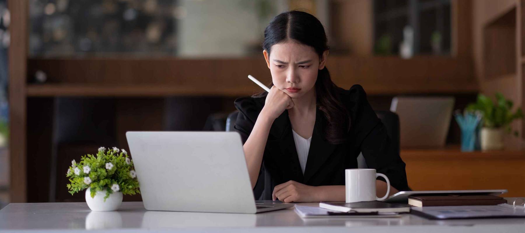 asian business woman thinking solving problem at work, worried serious young asian woman concerned make difficult decision lost in thought reflecting sit with laptop.