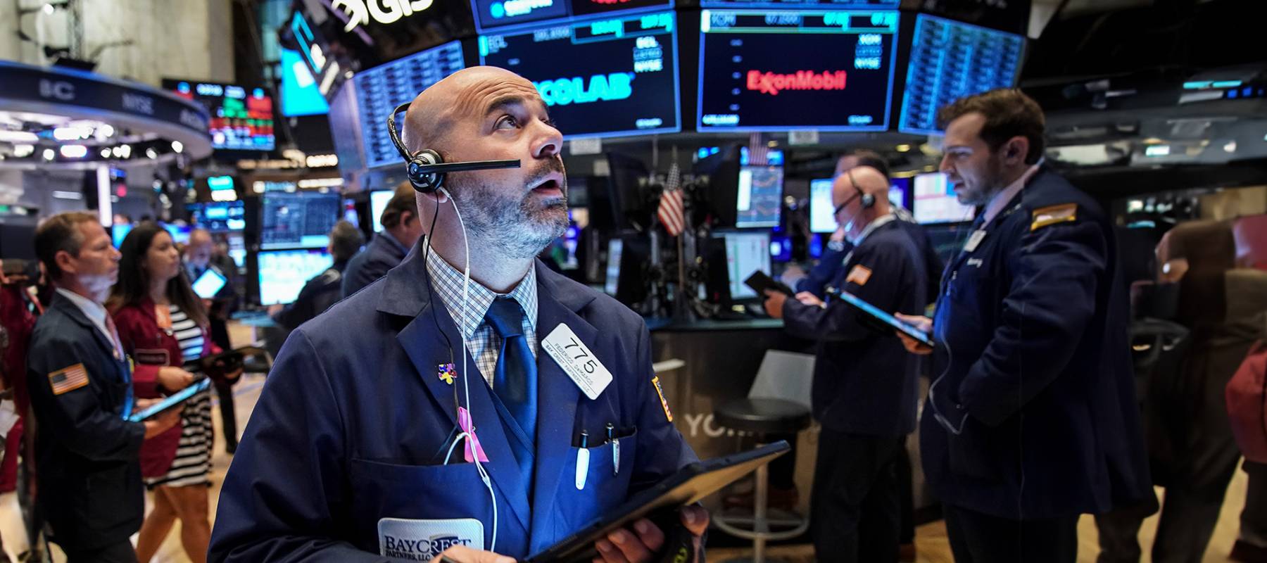 Broker on trading floor looking up with hustle and bustle of other brokers and many television and computer screen in background