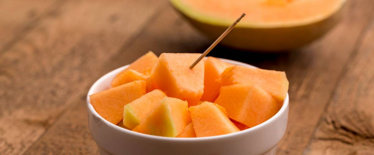 freshly cut muskmelon cubes in a white bowl with stick