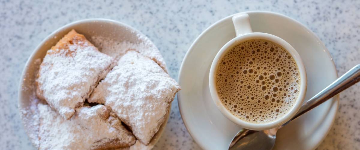 Beignets (French style donuts) topped with sugar and a cup of coffee in the background
