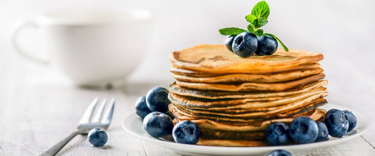 Pancakes with blueberries and mint leaf on top. Pile of small homemade pancakes with forest fruits. Heap of flat thin cake in background.