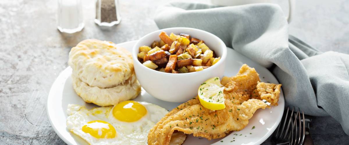 Fried fish breakfast with sunny side up eggs, biscuit and potatoes