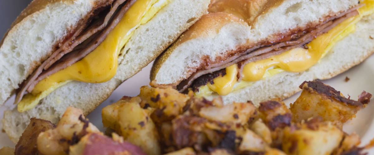 Taylor ham, pork roll, egg and cheese breakfast sandwich on a kaiser roll with salt pepper and ketchup and a side of home fries from New Jersey.