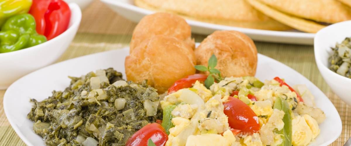 Traditional Jamaican dish made of salt cod and ackee fruit. Served with callaloo and johnny cakes. Patties on background.