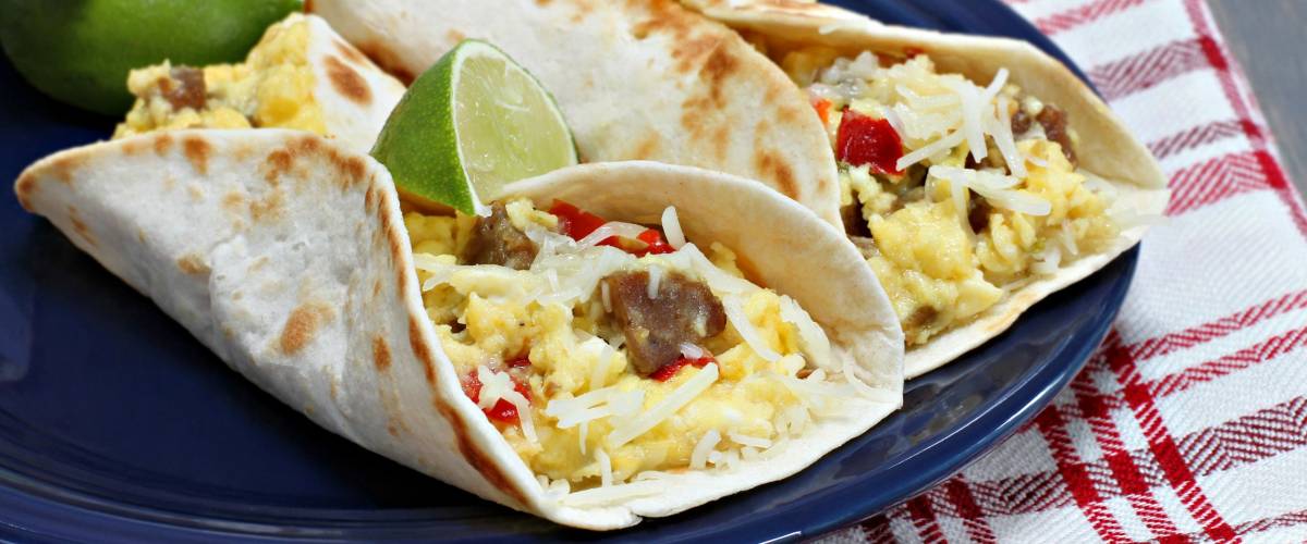 Two breakfast tacos with sausage, cheese, and peppers.Garnished with fresh lime.