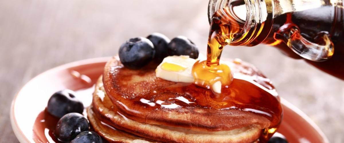 Pouring maple syrup on stack of pancakes