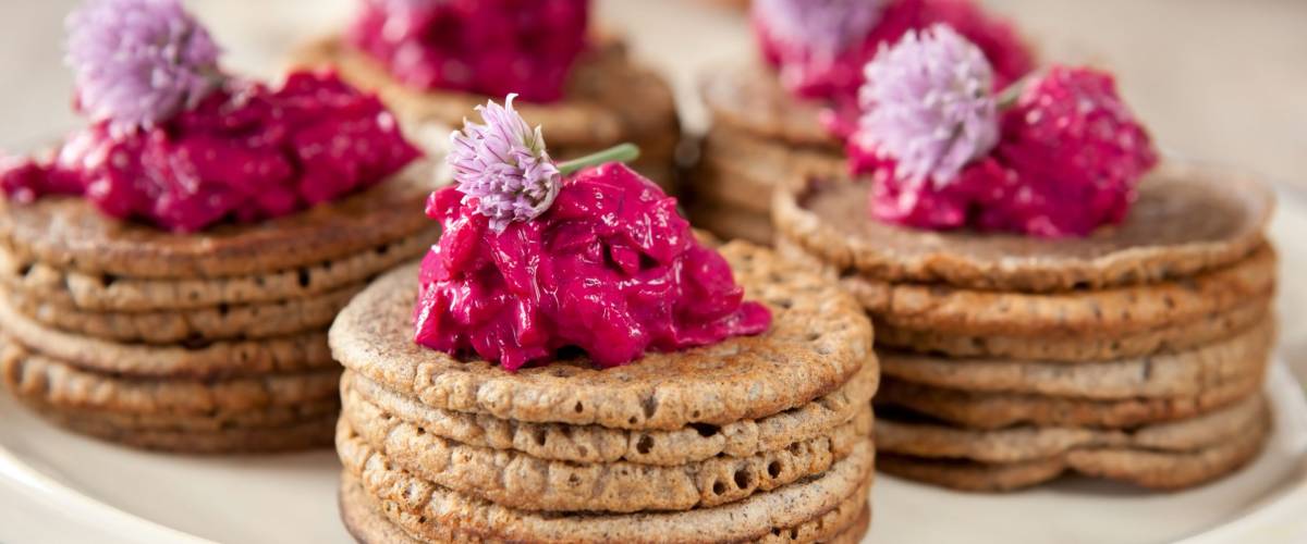 Mini buckwheat pancakes garnished with colorful beet salad and chives blossoms