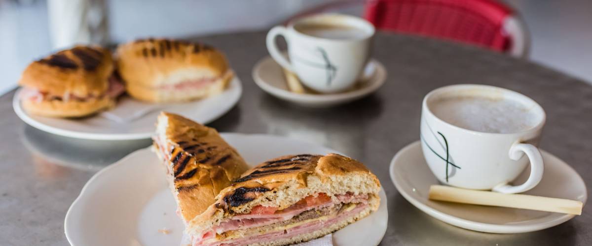 Authentic Cuban Sandwich grilled with layered ham, cheese, tomatoes, and pickles.