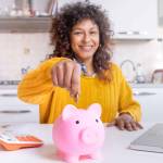 Smiling black woman saving goal for future retirement plan, focus on piggy bank
