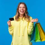 Carefree emotive, smiling happy pretty blond girl using credit card to waste some money in mall, holding shopping bags, buy gifts or presents, treat yourself day, laughing joyfully