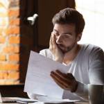 Confused frustrated young man reading letter in cafe, debt notification,