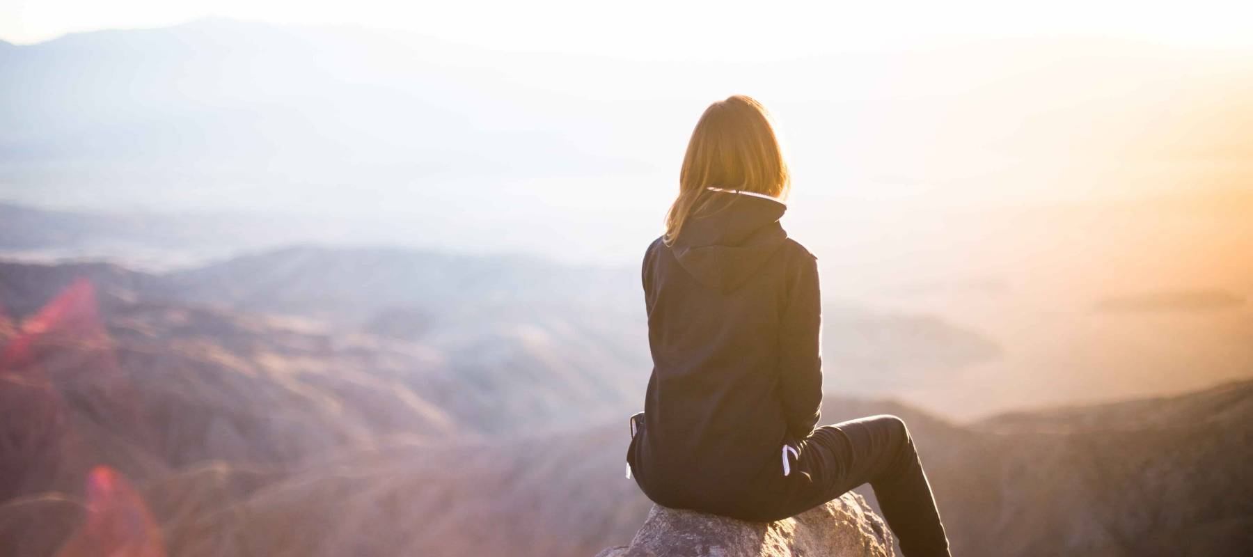 Woman sitting on mountain top making long term financial goals after paying off all her debt