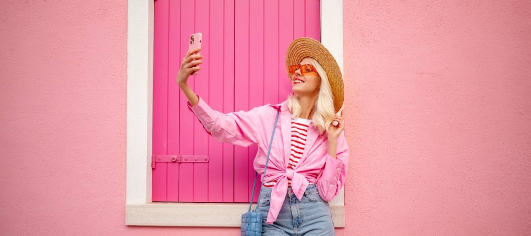 Happy young woman poses for a selfie in front of a pink house.