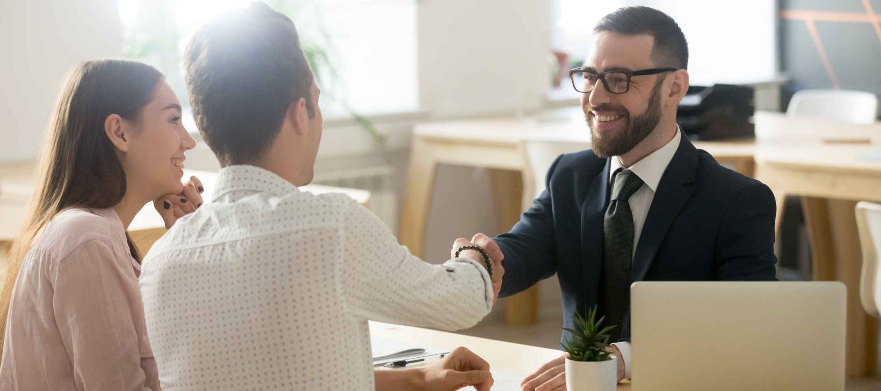 Smiling financial advisor handshaking young couple thanking shake hands making deal,