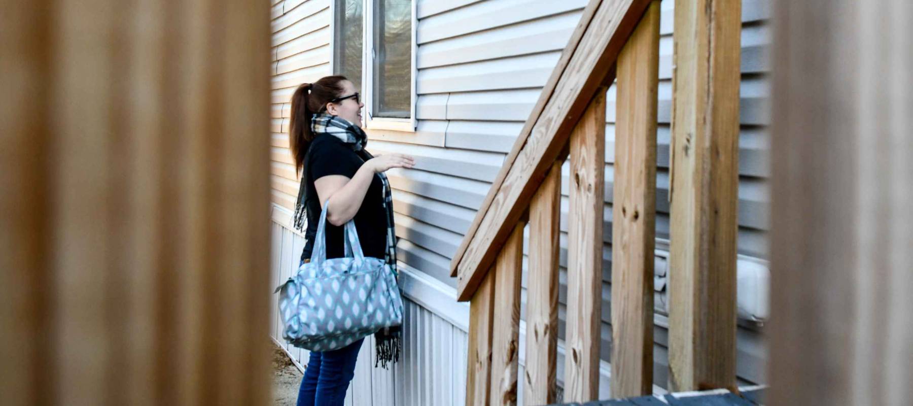 Woman looks into a window of a mobile home next to the front porch steps making a funny face to who is on the other side.