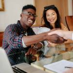 Happy property owners shaking hands with real estate broker after a deal. Young couple handshaking real estate agent after signing contract.