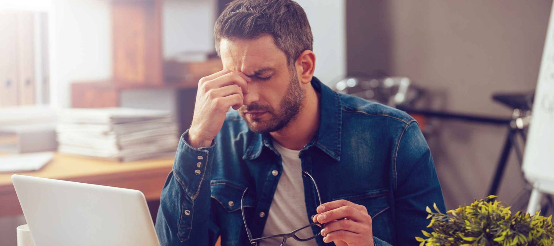 Feeling sick and tired. Frustrated young man massaging his nose and keeping eyes closed while sitting at his working place in office